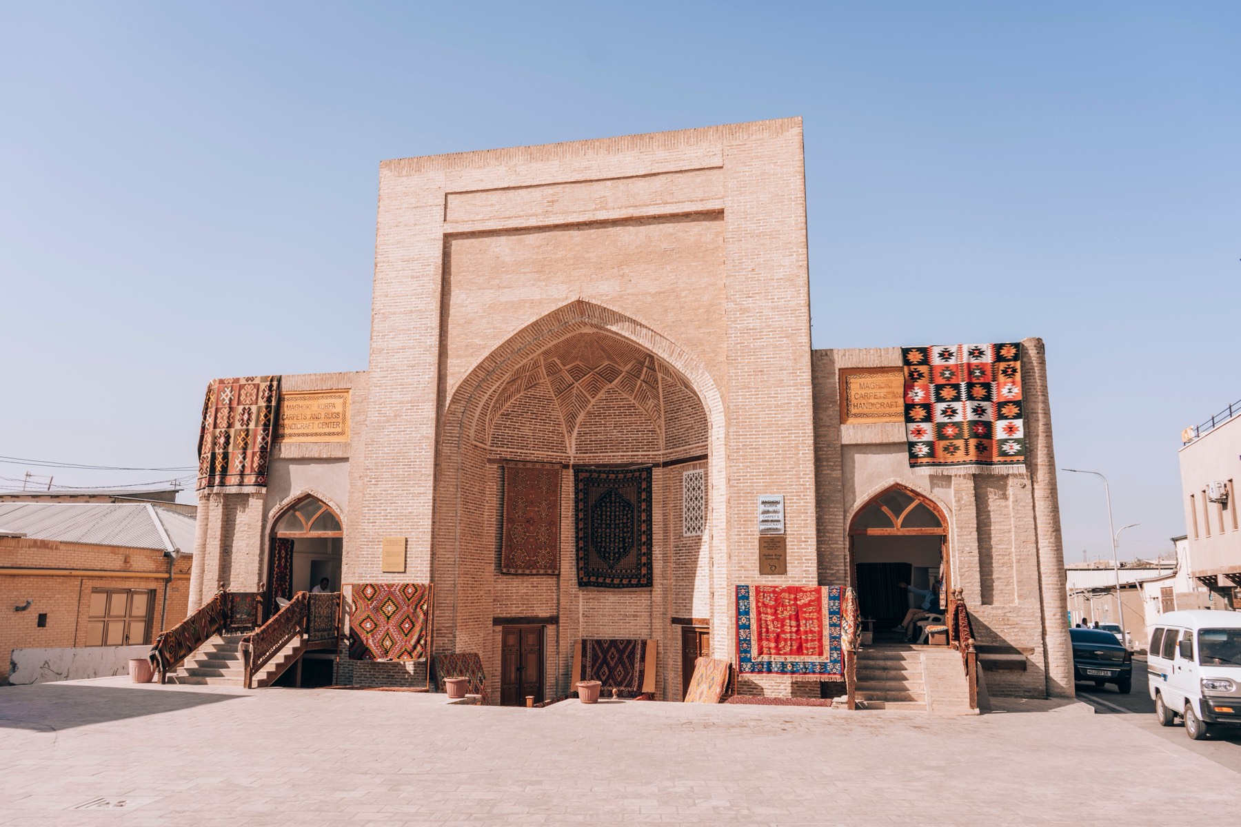 A restored caravanserai in Bukhara's old town with hand-woven carpets and suzani hung across its brick facade.
