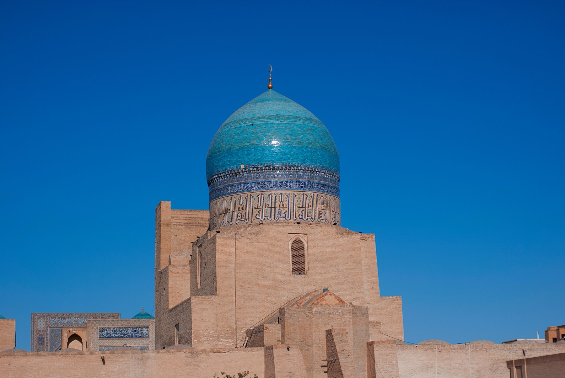 The turquoise mosaic dome of the Kalyan Mosque against a cloudless deep blue sky.